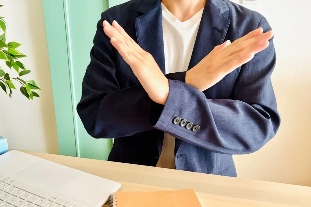 パソコンの前でバツサインを出す男性