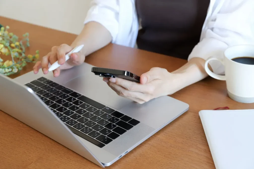 スマートフォンを見ながらパソコンを操作する女性