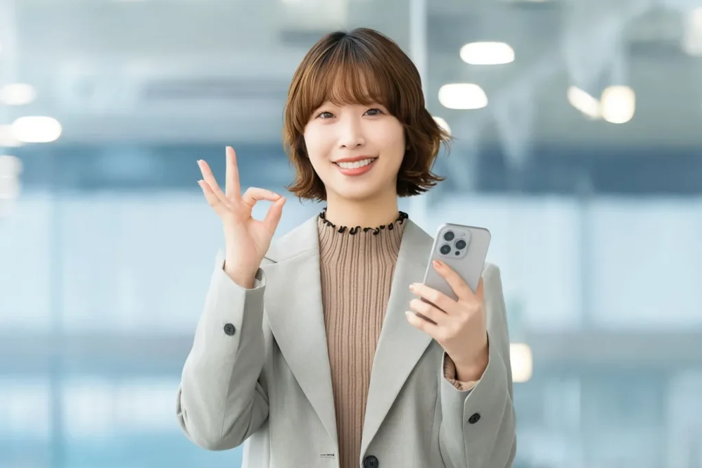 スマートフォンを持ってOKサインを出しているビジネスウーマン